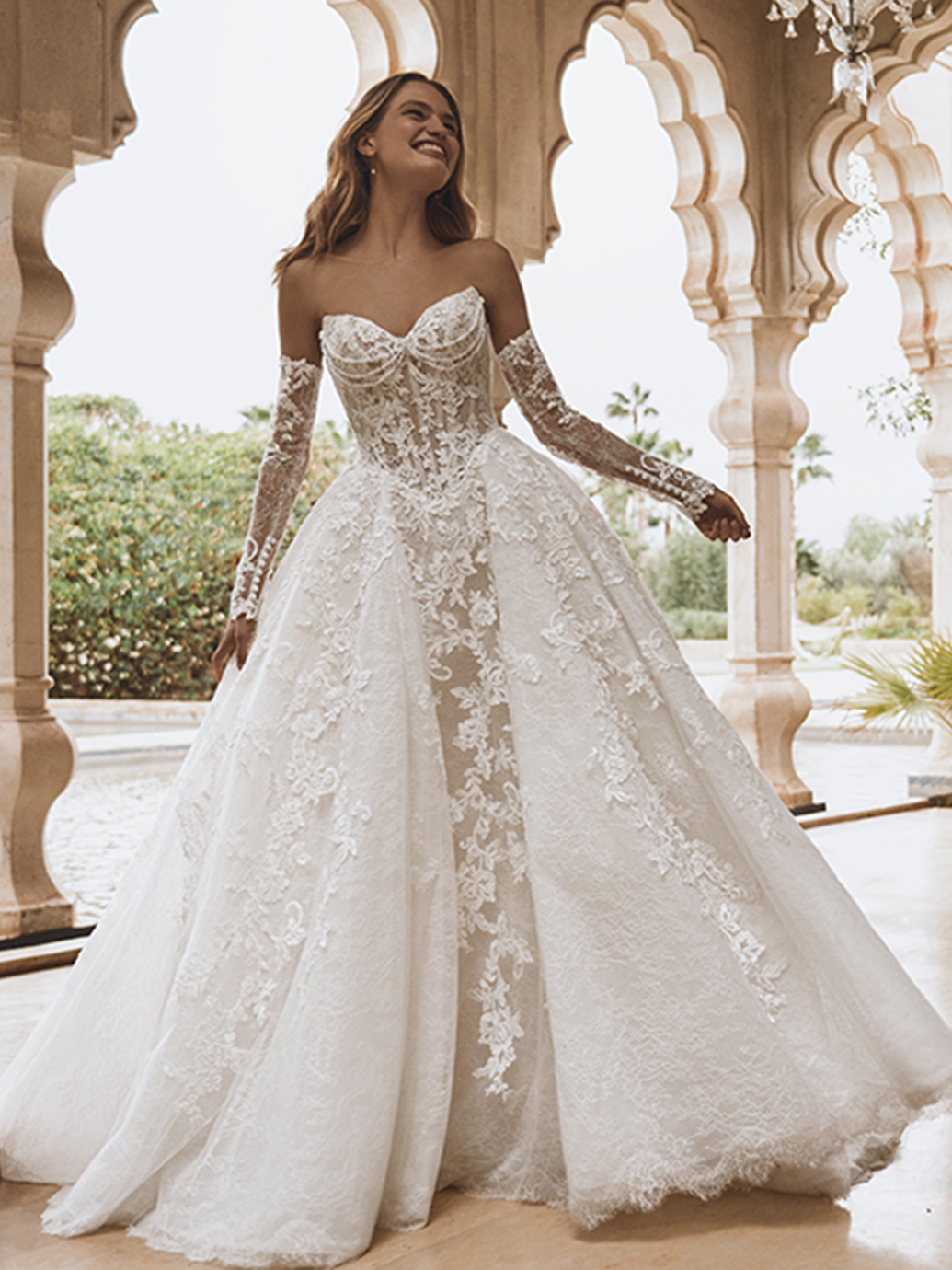 Stunning lace ball gown with sheer off-shoulder sleeves — available at Be Unique Boutique, Mount Kisco NY